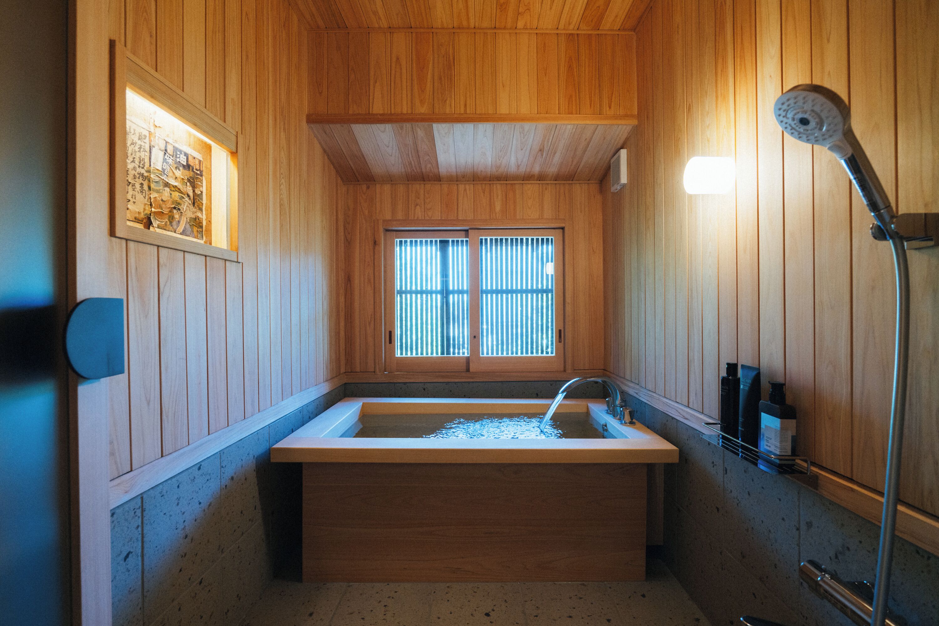 Un intérieur en bois avec une grande baignoire, une fenêtre avec des stores et une pomme de douche.