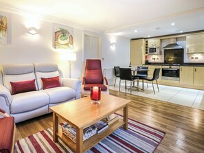 A modern living room with a sofa, armchairs, a coffee table, and a dining area with chairs and a table. There is a kitchen with appliances and a microwave. - 2 bedroom accommodation in Bath (Bath)