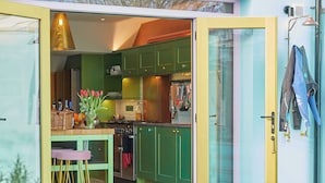Une cuisine avec des meubles de couleur verte, une porte jaune et un coin repas comprenant une table et des chaises.