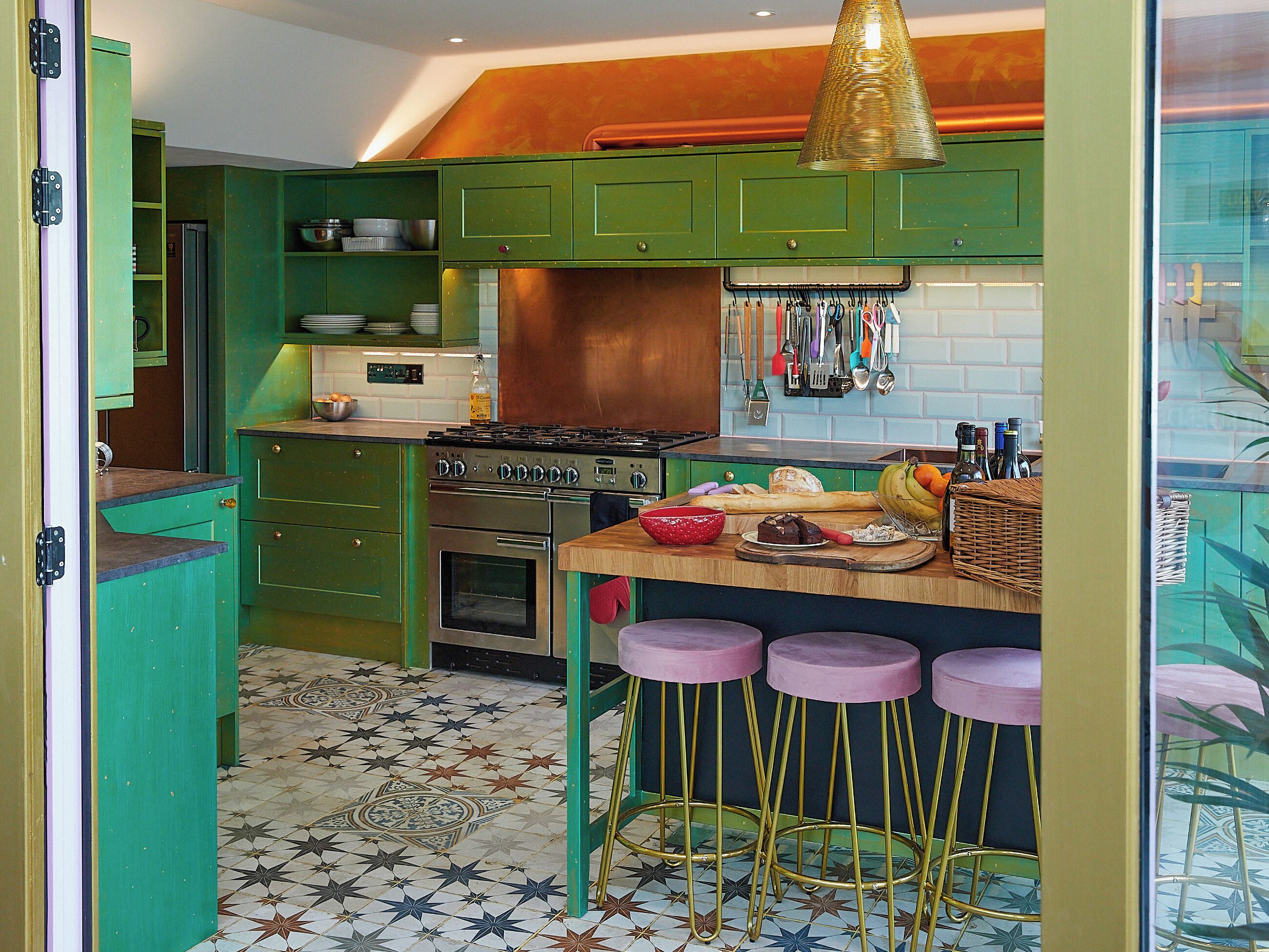 Una cocina con gabinetes verdes, una estufa a gas, un lavamanos y una barra con taburetes.
