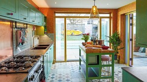Une cuisine avec des meubles de rangement verts, un sol carrelé et un coin repas avec une table mise pour deux personnes.