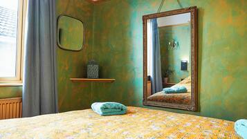 A room with a bed, a mirror, a shelf with a lantern, and a window with curtains.