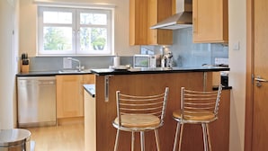 A modern kitchen with wooden cabinets, a stainless steel dishwasher, a microwave, and two bar stools.