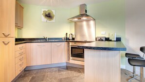 Een moderne keuken met houten kastjes, een rvs afzuigkap, een marmeren vloer en een bar met barkrukken.