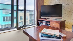 Een moderne woonkamer met een groot raam, een flatscreen-televisie, een houten salontafel en een boekenkast.