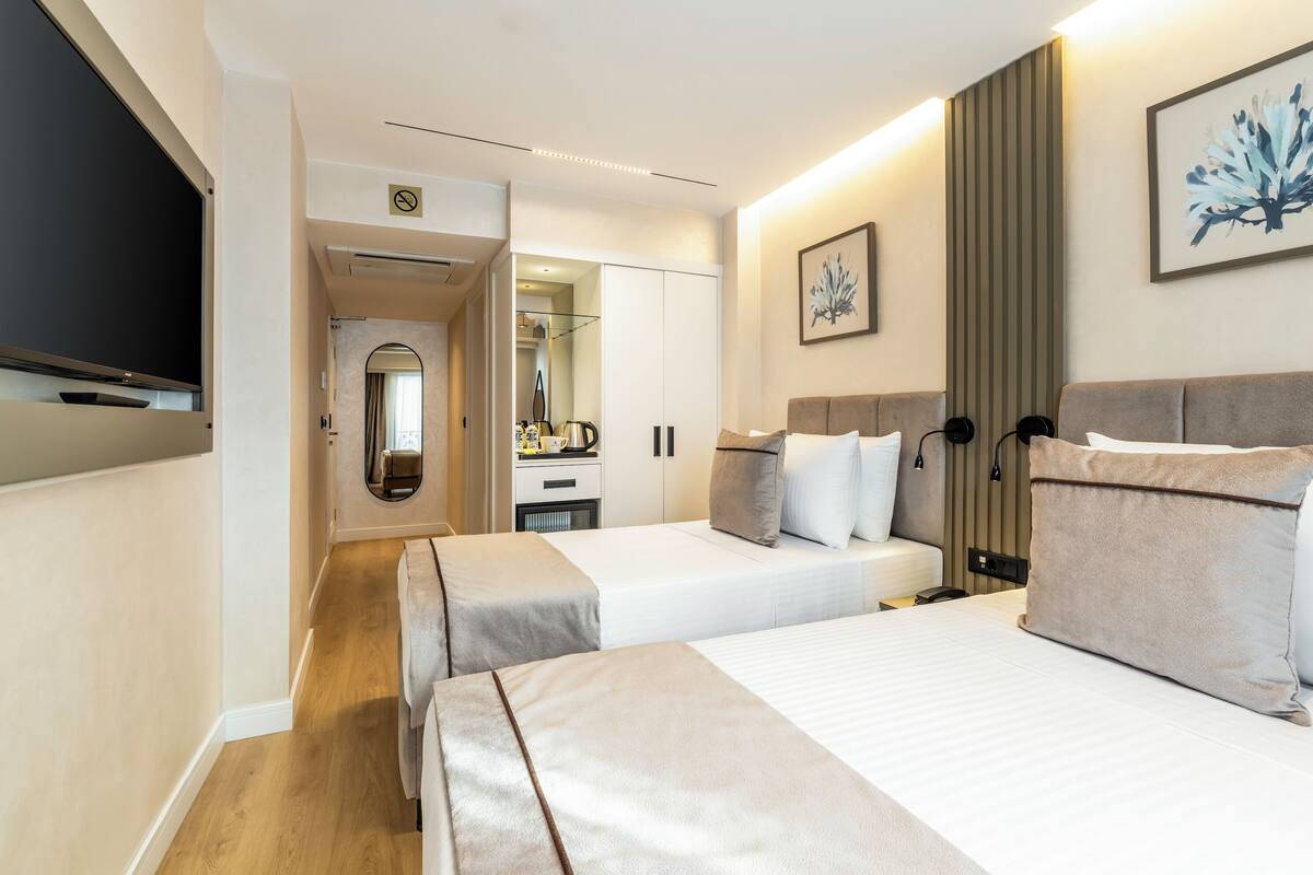 A hotel room with two beds, a TV, a mirror, and a kitchenette.