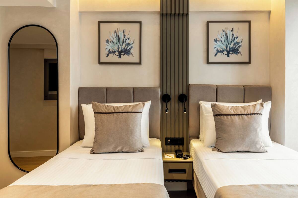A hotel room with two beds, a mirror, and artwork on the walls.