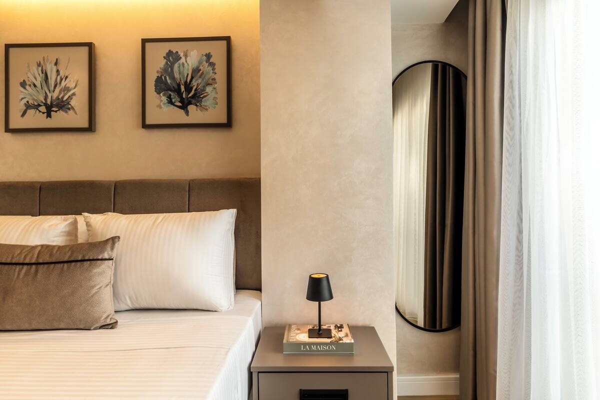 A neatly made bed with a pillow, a bedside table with a lamp, and two framed artworks on the wall.