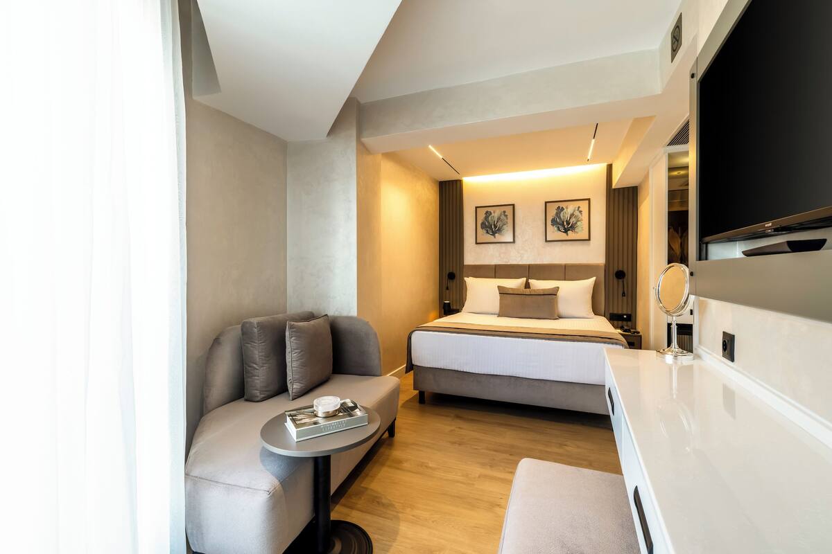 A compact hotel room with a bed, a sofa, a small table, and a TV.