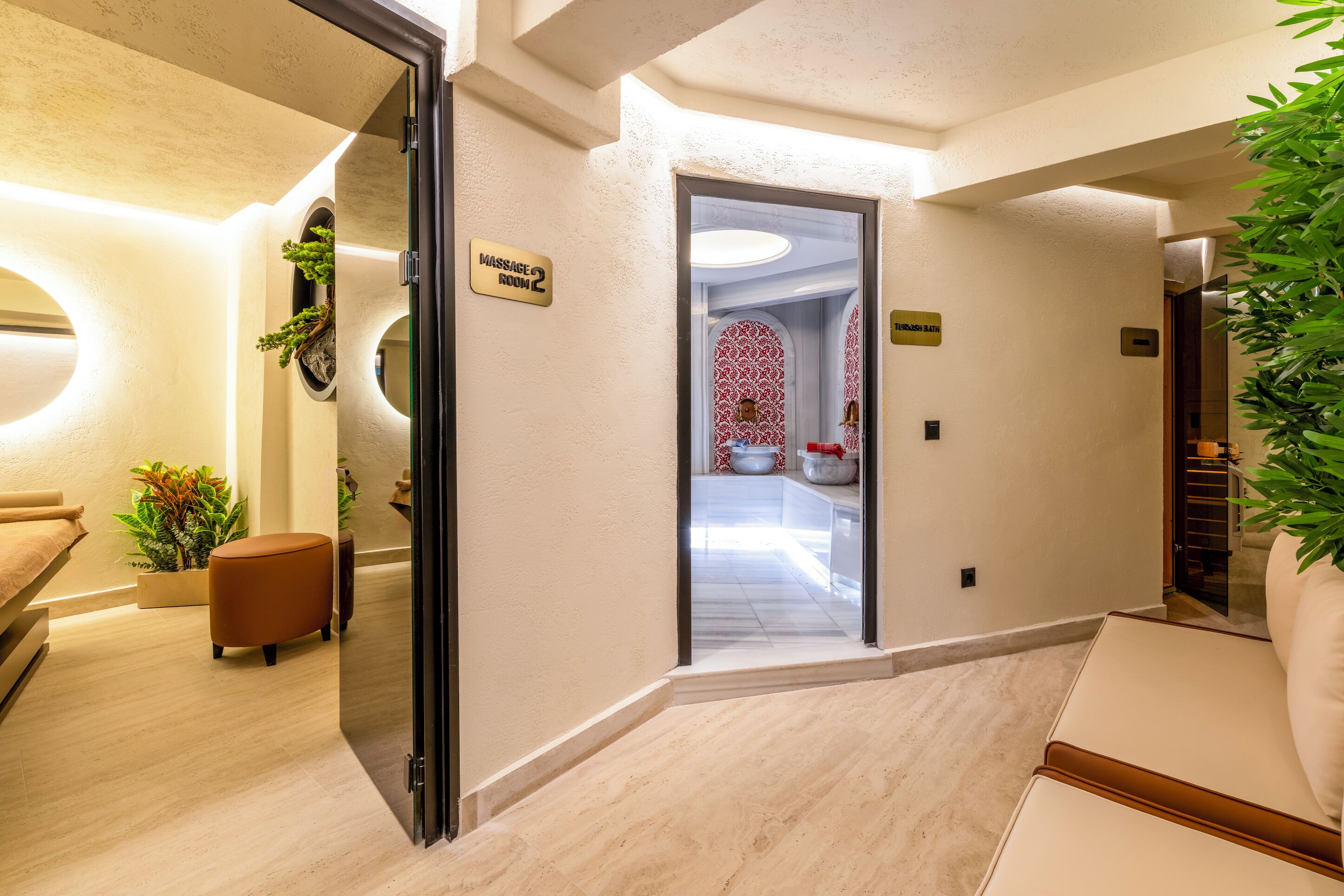 Pasillo de hotel con letrero de sala de masajes, mostrador de recepción y una planta.