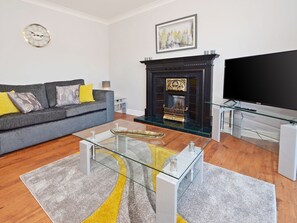 Ein modernes Wohnzimmer mit einem grauen Sofa, einem Glastisch, einem Kamin und einem Flachbildfernseher.