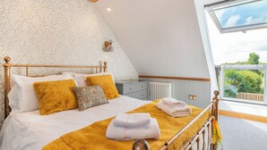 Een slaapkamer met een bed, nachtkastje, radiator, raam en uitzicht op groen.