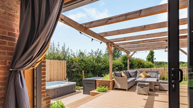 Een terras buiten met een jacuzzi, zithoek en een houten pergola.