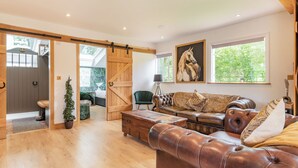 Een ruime woonkamer met houten vloer, een leren bank, een houten salontafel en een schuifdeur van hout die naar een andere kamer leidt.