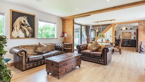 Een ruime woonkamer met lederen banken, een houten salontafel en een groot schilderij van paarden.