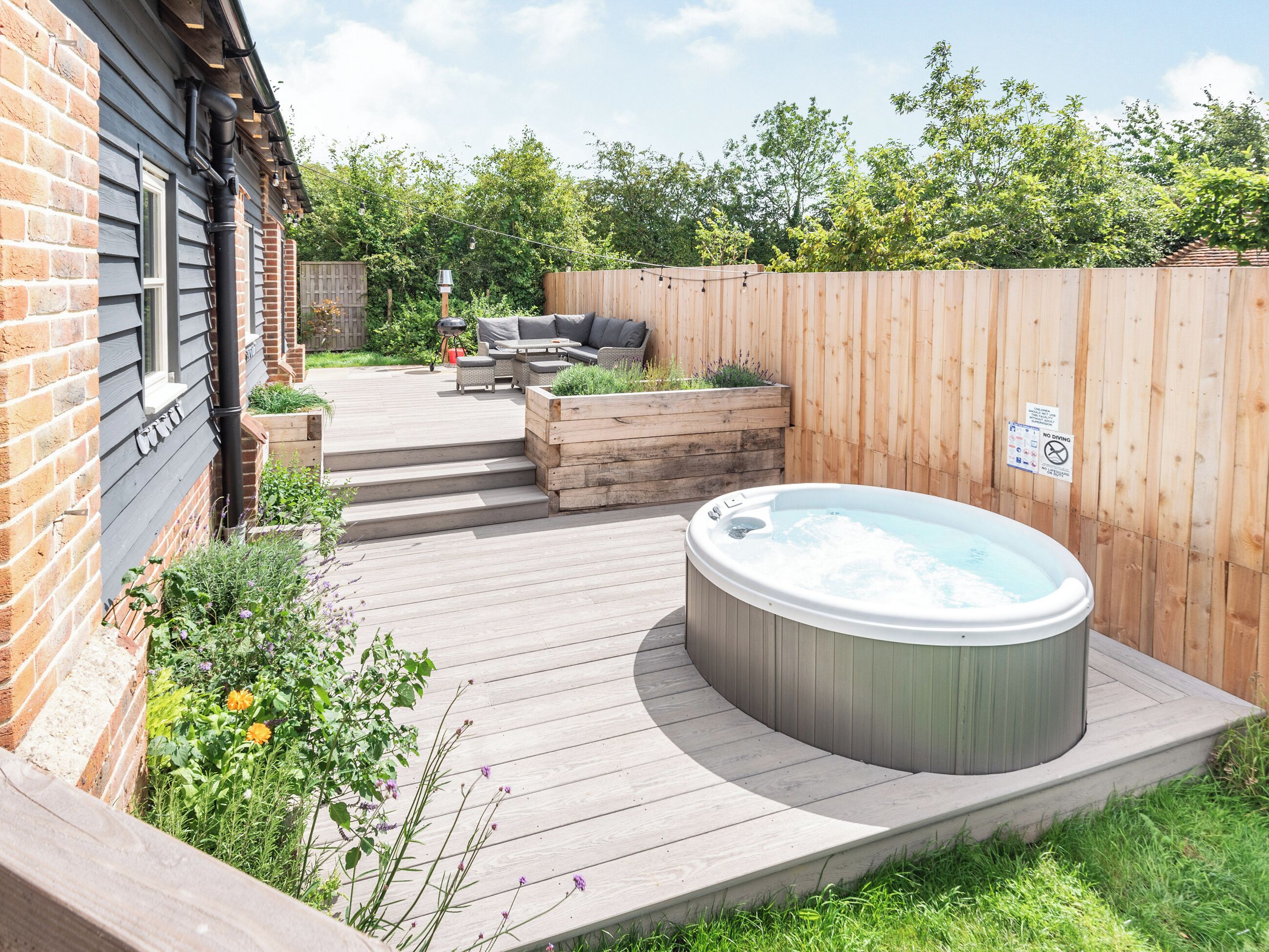 Un patio trasero con jacuzzi, terraza de madera, mobiliario exterior y una casa de ladrillo.
