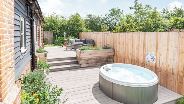 En trädgård med en bubbelpool, ett trädäck, utemöbler och ett hus byggt av tegel.