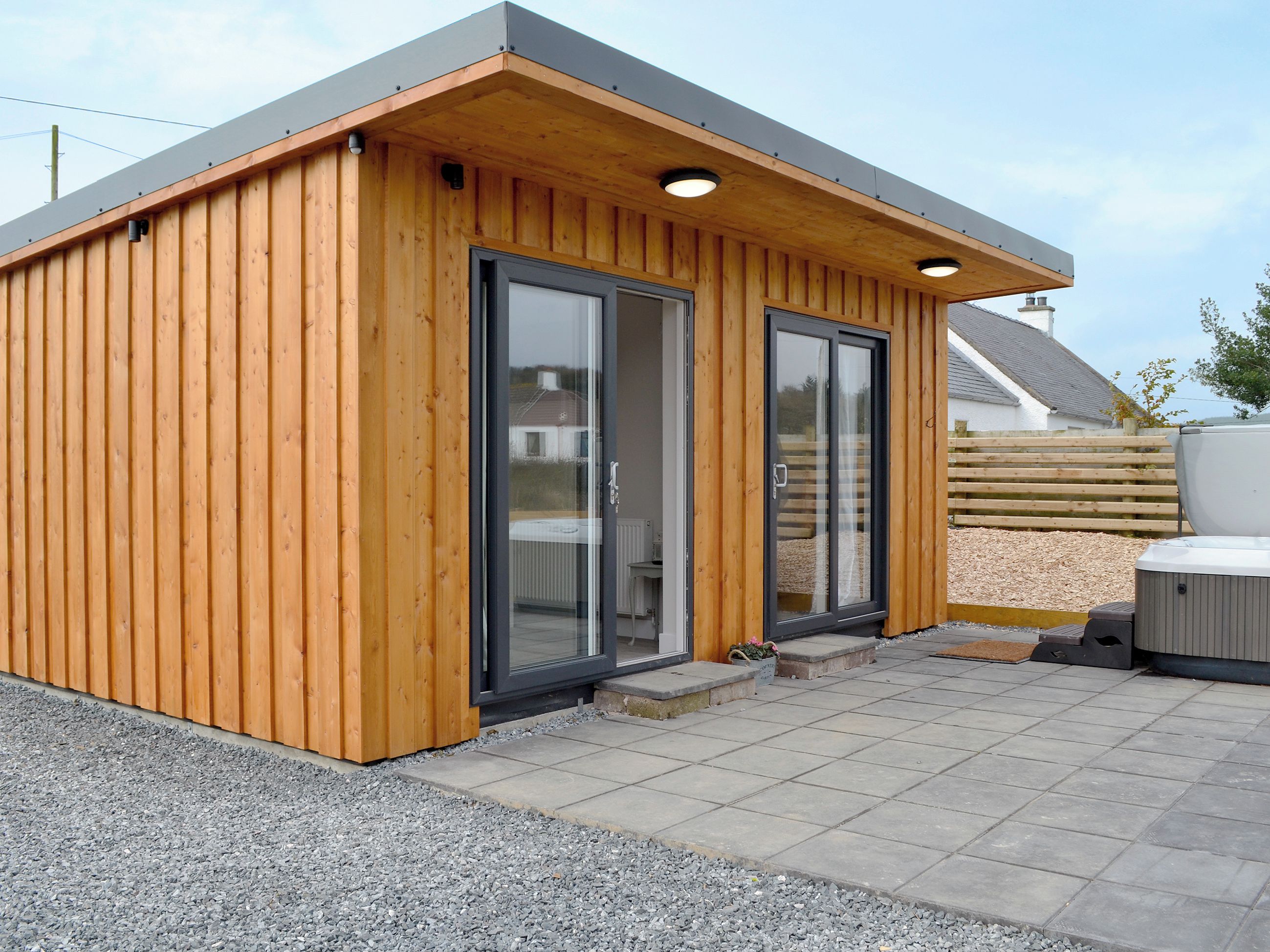Een klein houten huisje met een schuifdeur van glas, een terras en een hottub.