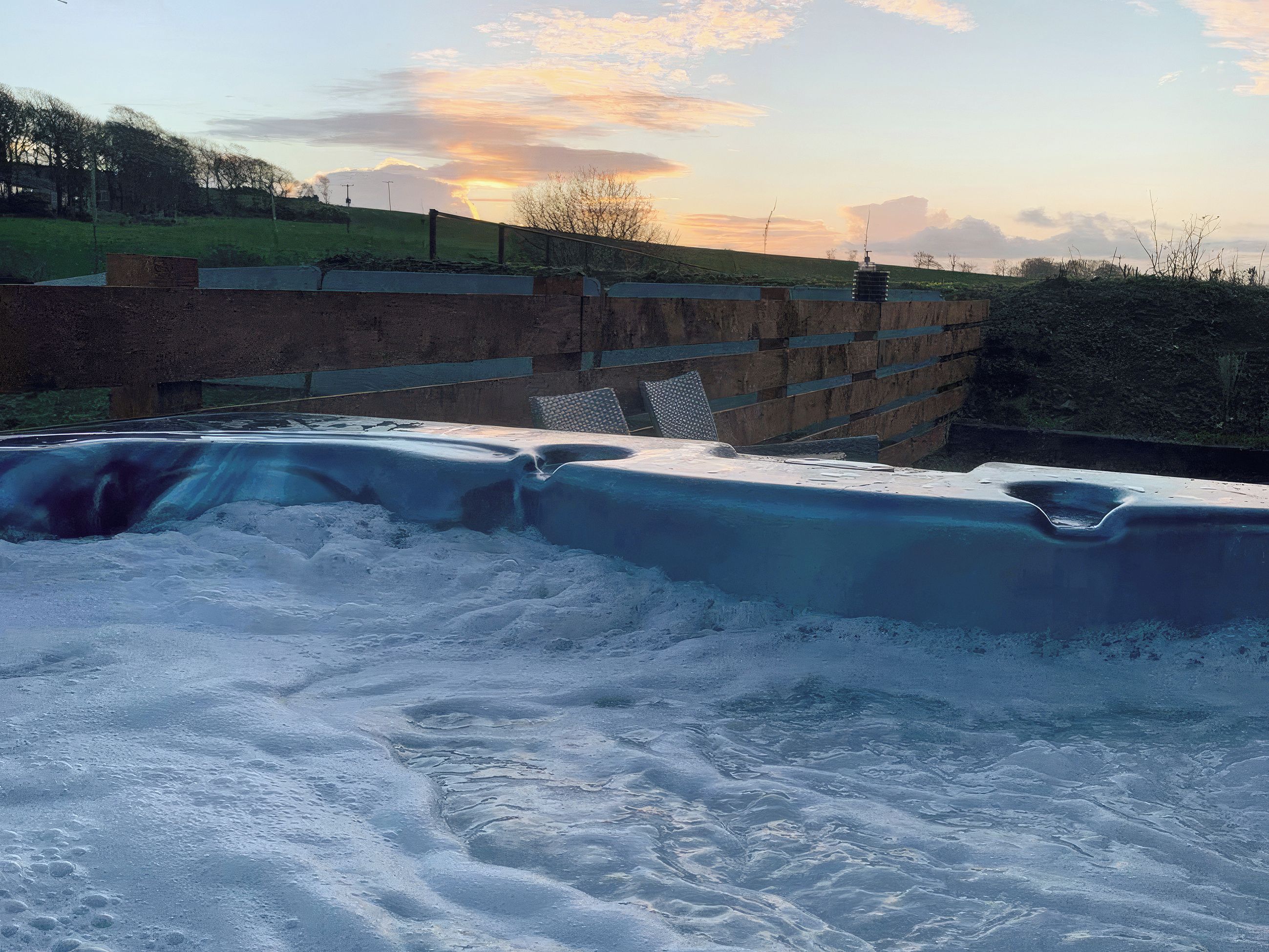 Een hottub met een houten omheining en een grasveld op de achtergrond.