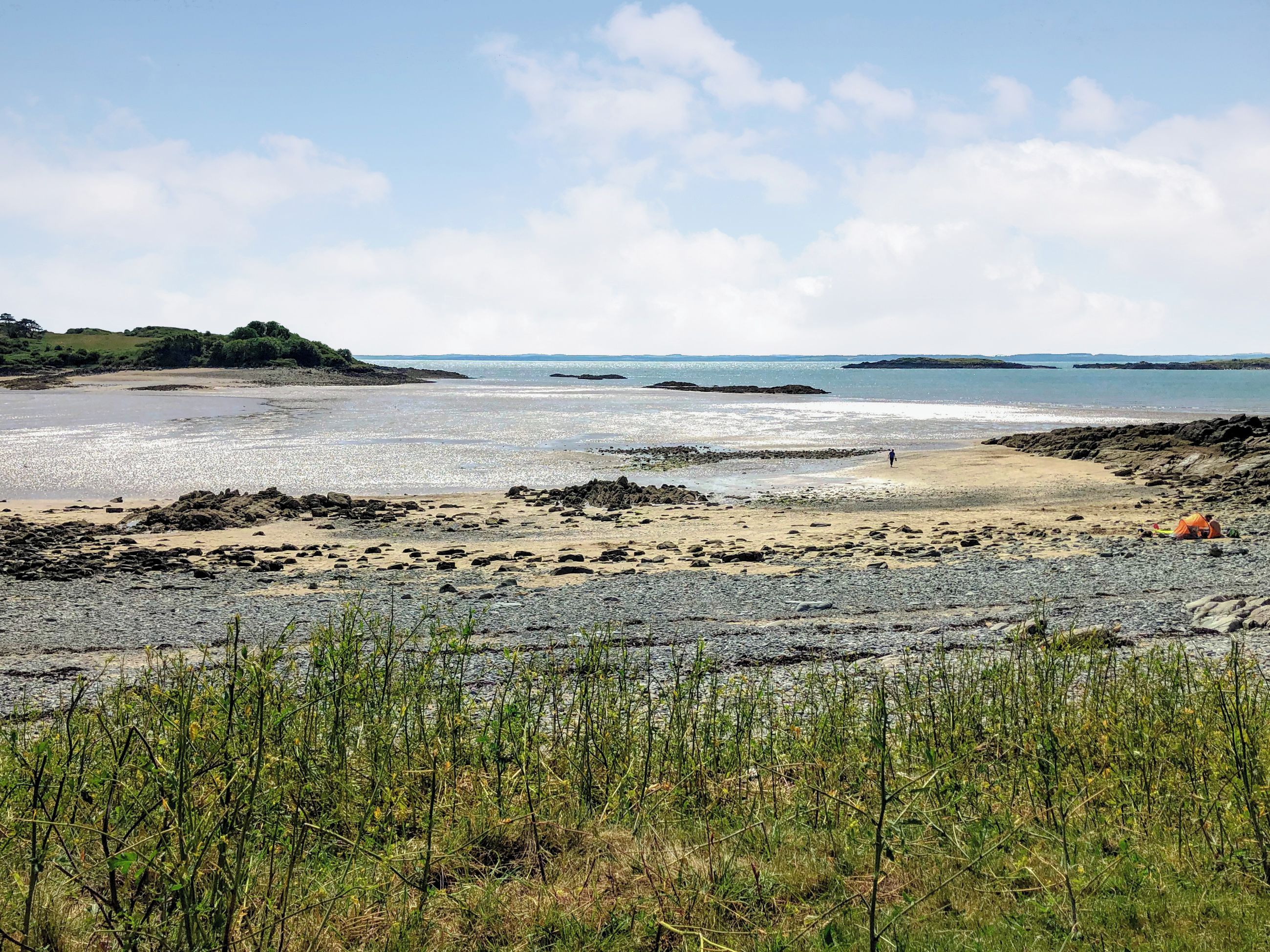A beach with rocky terrain, a tent, and a person walking.