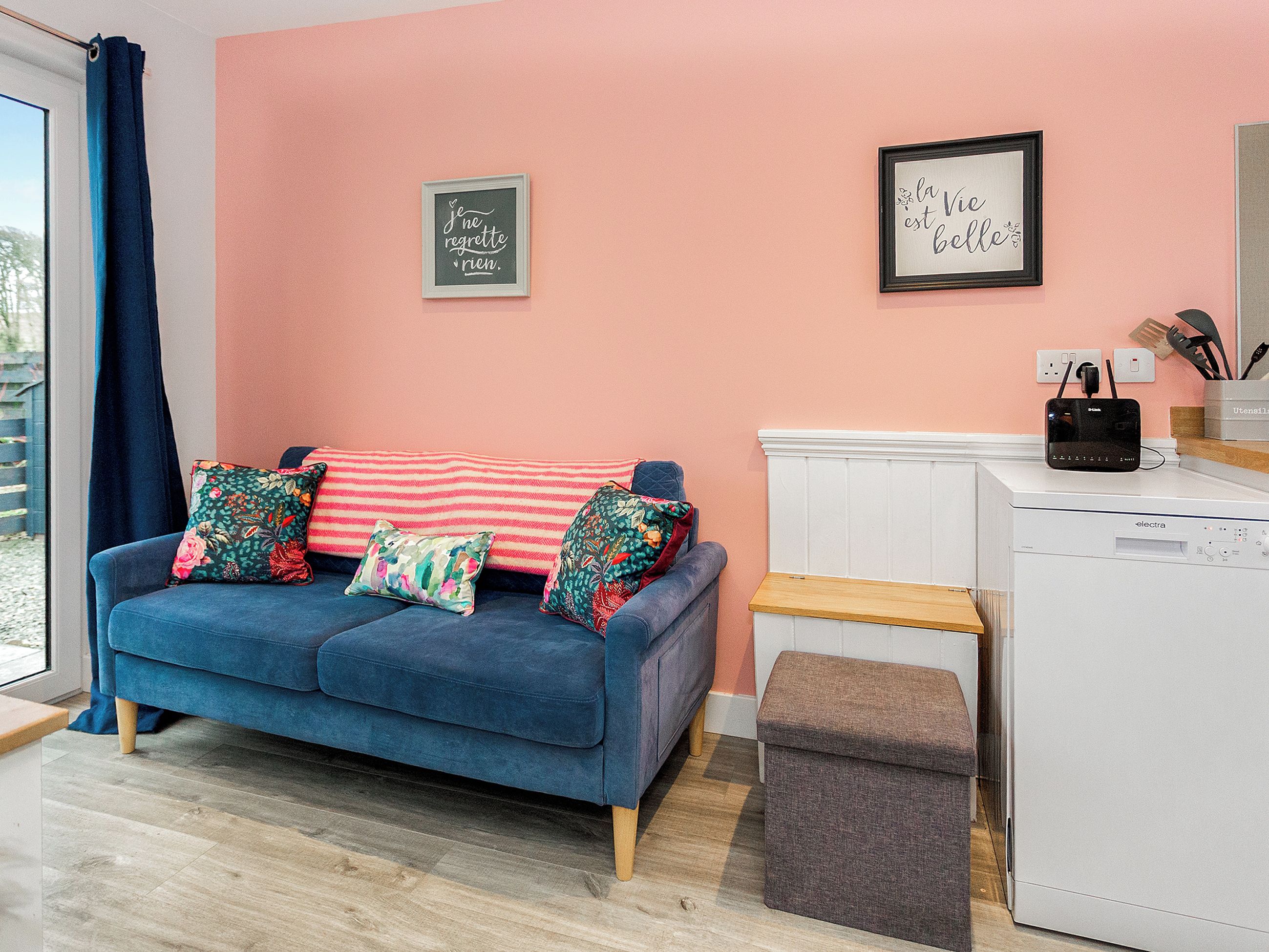 Een moderne woonkamer met een blauwe bank, decoratieve kussens, een roze muur en een wit apparaat.