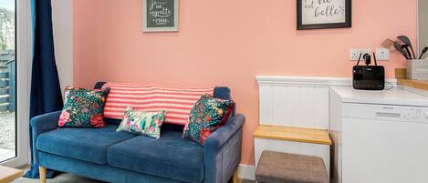 Een moderne woonkamer met een blauwe bank, decoratieve kussens, een roze muur en een wit apparaat.