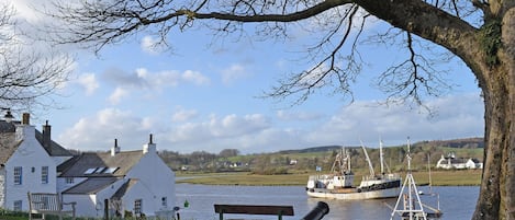 A white building with a sloped roof, a bench, and a cannon near a body of water.