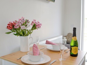 Ein Esstisch mit einer weißen Karaffe, einem Glas, einer Prosecco-Flasche und einer Schale mit einem karierten Servietttuch.