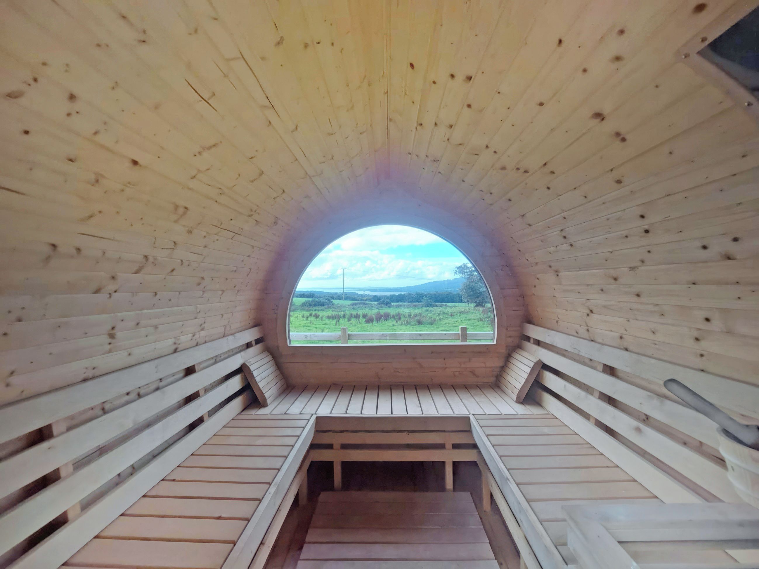 A circular wooden structure with a view of a green landscape through a large window.