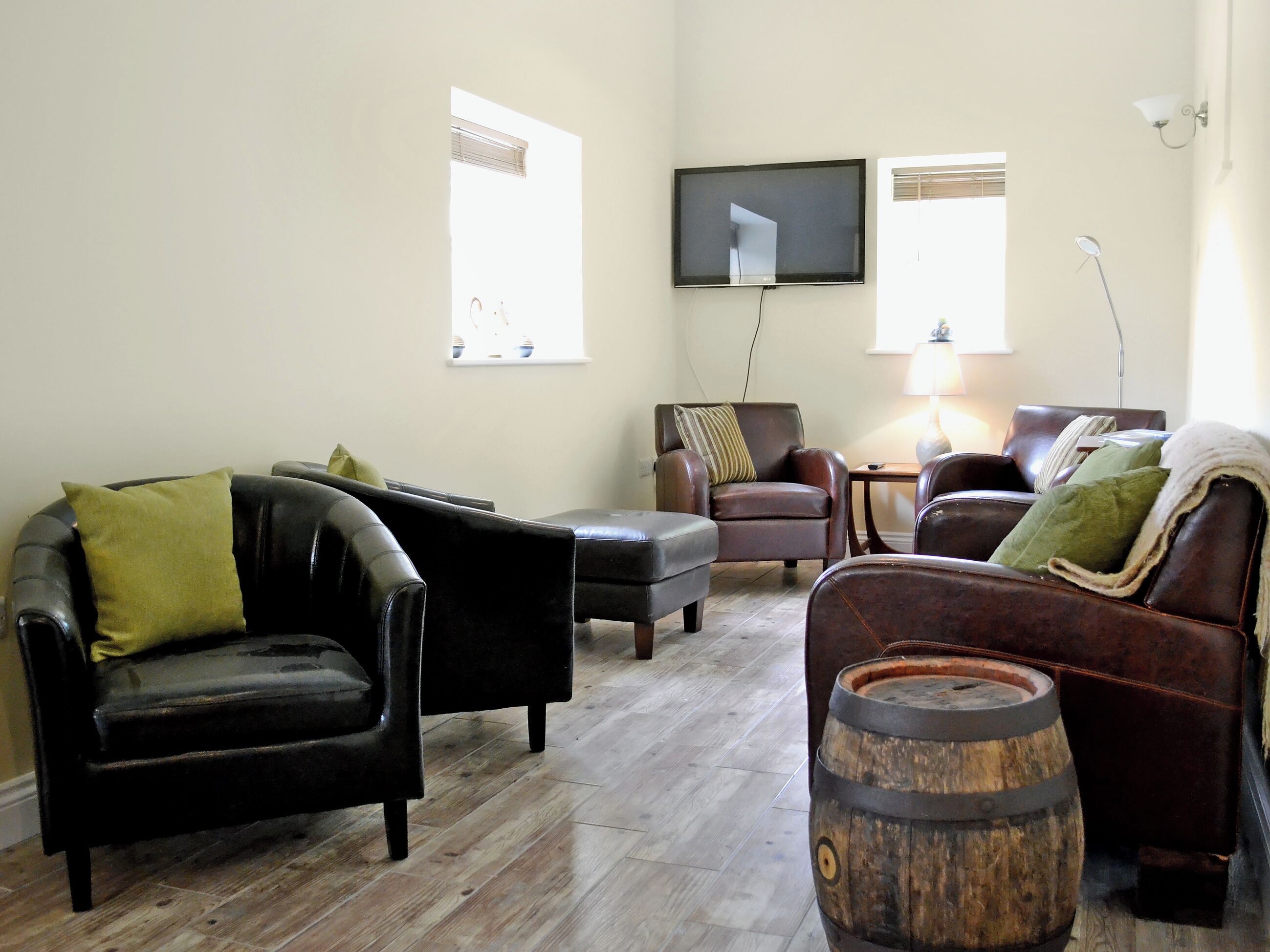 A living room with leather sofas, a wooden barrel, and a flat-screen TV mounted on the wall.