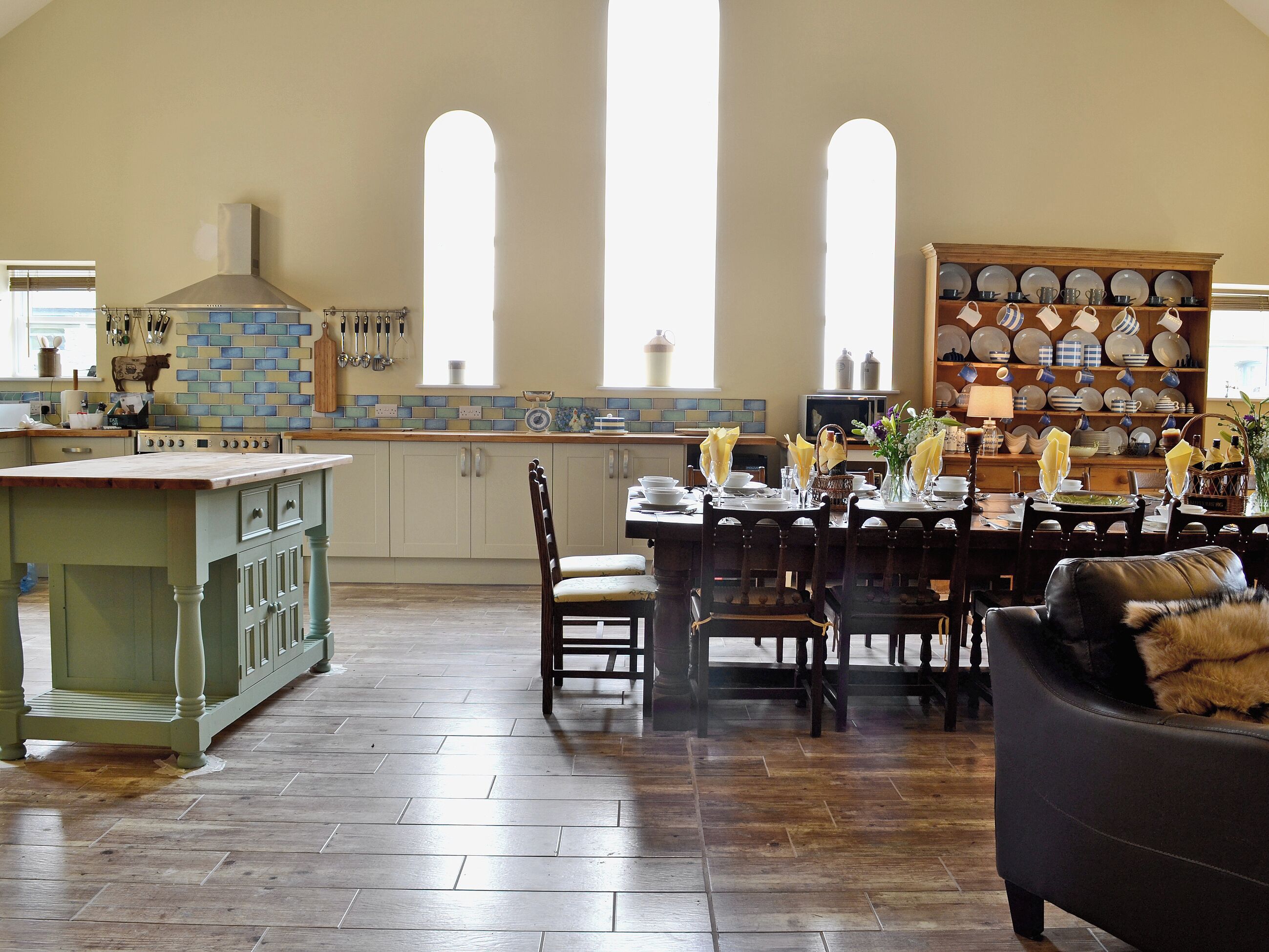 A spacious kitchen with a dining area, featuring a large island, wooden cabinets, and a tiled backsplash.
