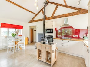 A kitchen with a wood beam ceiling, a stove, and a red backsplash.