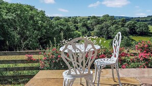 A patio with two white chairs and a table, surrounded by a wooden fence and a garden with pink flowers.