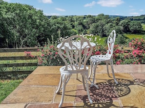 A patio with two white chairs and a table, surrounded by a wooden fence and a garden with pink flowers.