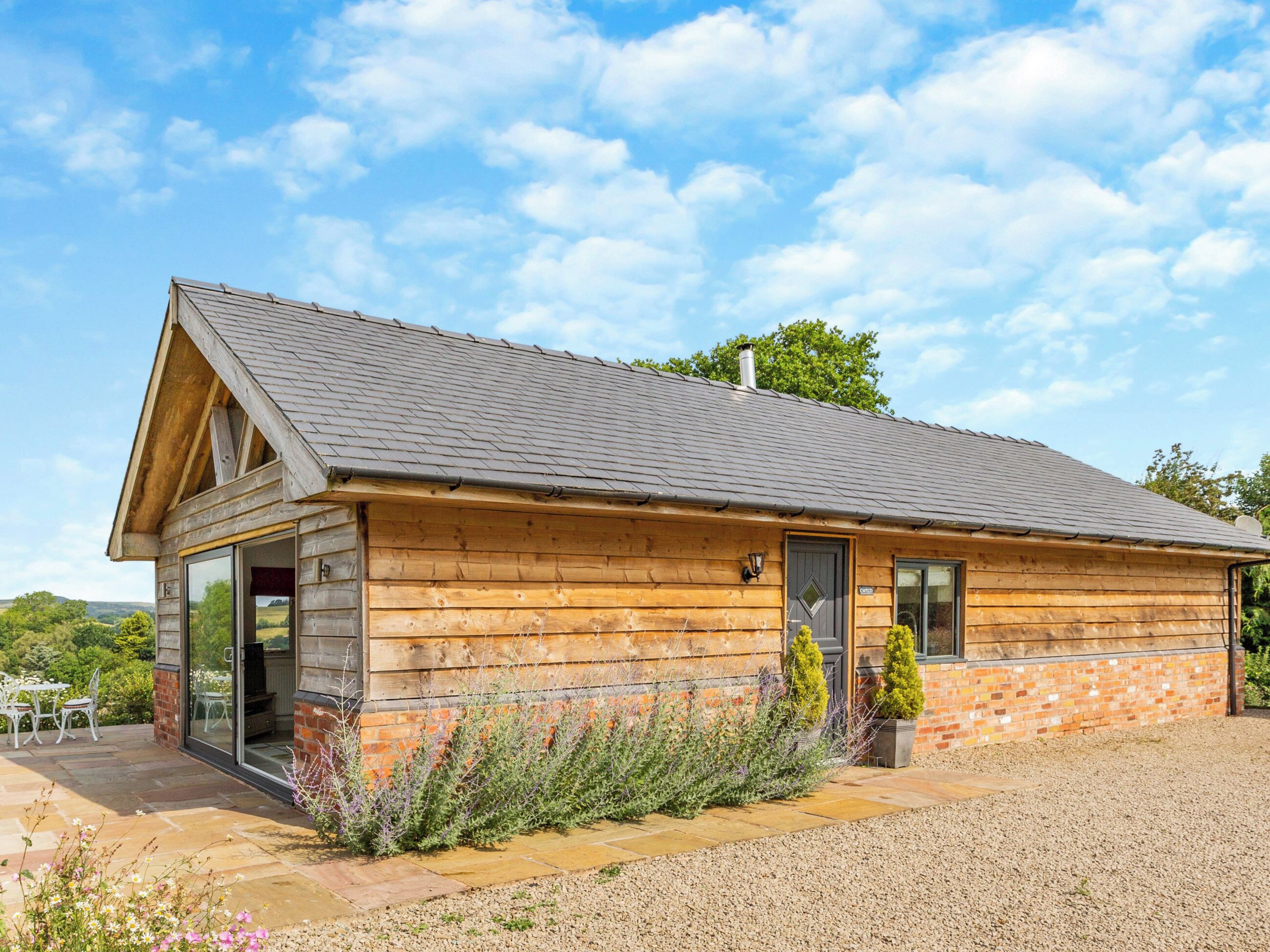 Une cabane en bois avec un toit en pente, une porte d’entrée en verre et une allée gravillonnée.