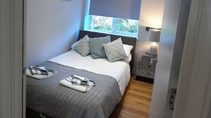 Ein Schlafzimmer mit einem Bett, Kissen, einem Nachttisch mit Lampe und einem Fenster mit Jalousien.
