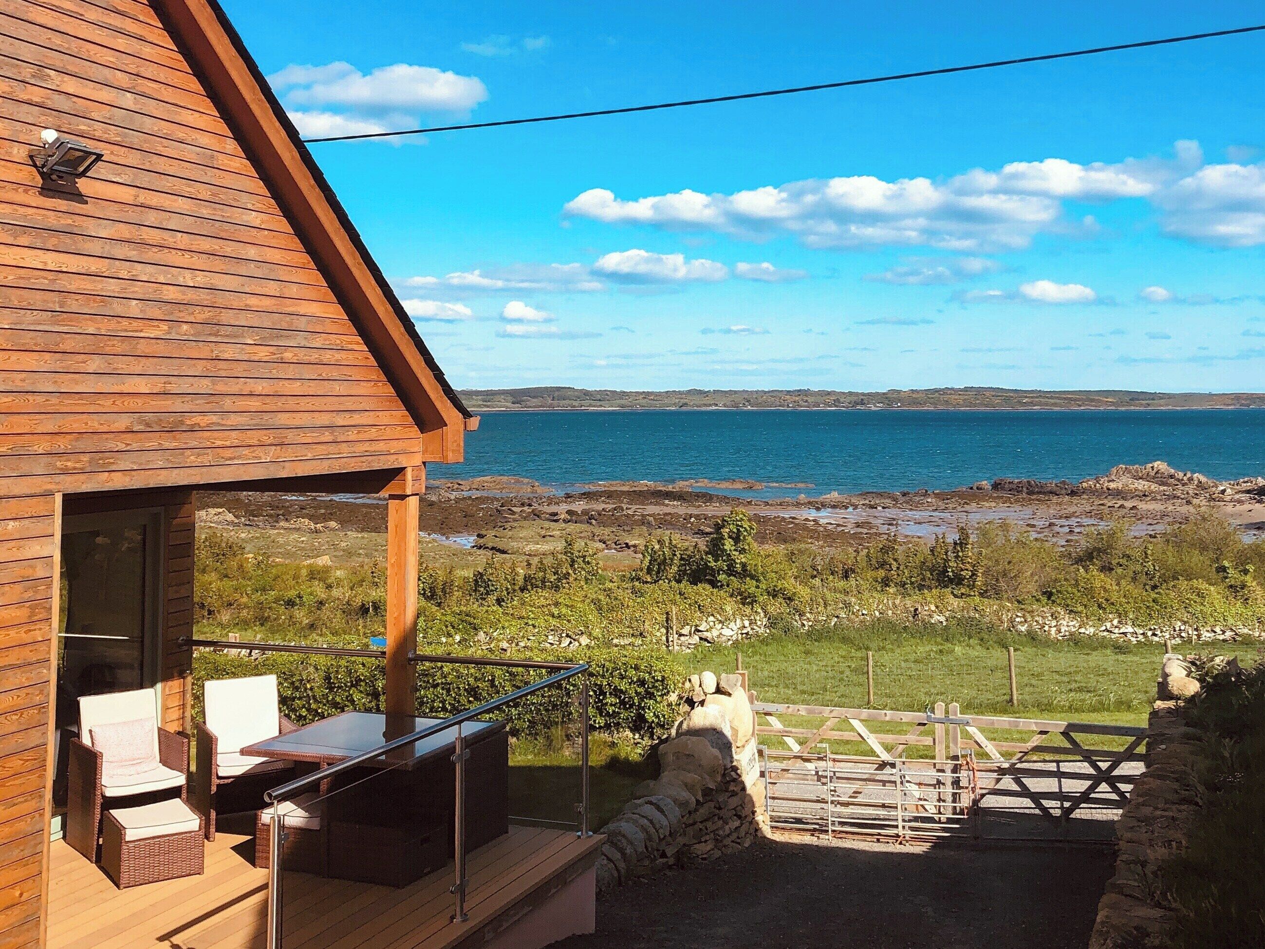 Un bâtiment en bois doté d’un balcon donnant sur une côte rocheuse et un ciel bleu dégagé.