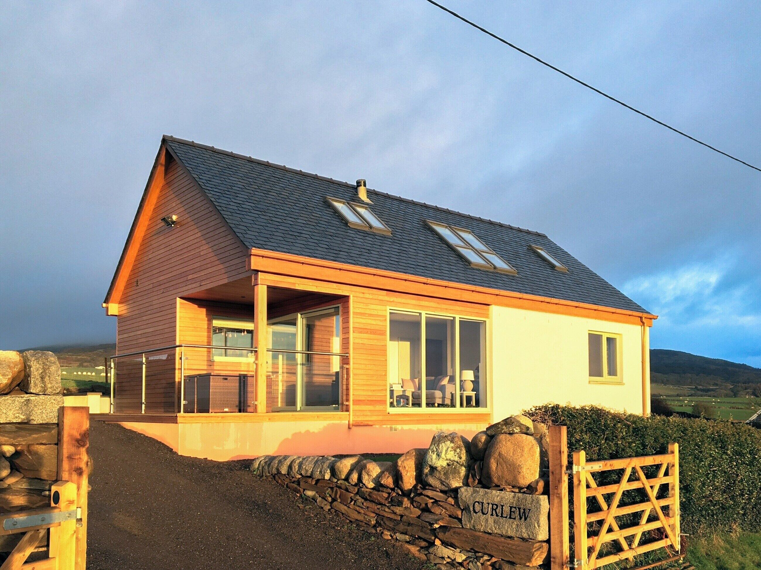 A modern house with a stone wall entrance, large windows, and a nameplate reading "CURLEW".
