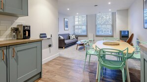 Eine moderne Küche mit Kaffeemaschine, ein Essbereich mit Tisch und Stühlen sowie ein Wohnzimmer mit Sofa und Fernseher.