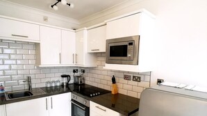 A compact kitchen with white cabinets, a stainless steel microwave, a built-in oven, and a refrigerator. - Gloucester Apartment - UK37842 (Bristol)
