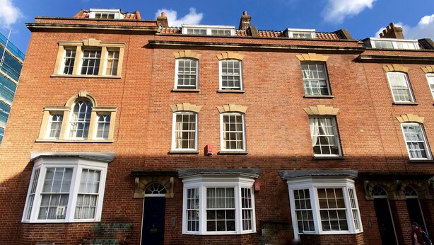 A red brick building with multiple windows, a dark blue door, and a small garden area. - Gloucester Apartment - UK37842 (Bristol)