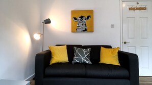 A black sofa with yellow and white pillows, a floor lamp, and a wall-mounted artwork. - Gloucester Apartment - UK37842 (Bristol)