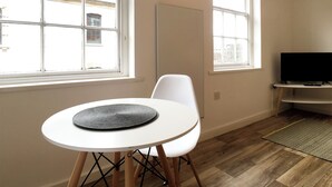 A room with a round white table, a white chair, a TV on a stand, and large windows with a view of buildings outside. - Gloucester Apartment - UK37842 (Bristol)
