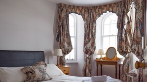 A bedroom with a bed, two bedside tables, a mirror, and floral curtains. - Castle Peroch-UK5698 (By Dunkeld, Pitlochry)