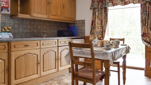 Een keuken met houten kastjes, een eettafel met stoelen en een raam met gordijnen.