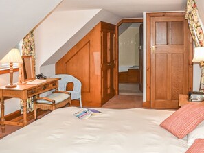 Ein Schlafzimmer mit einem Bett, einem Schreibtisch mit Lampe, einem Stuhl, einem Kleiderschrank und einer Tür zu einem anderen Raum.