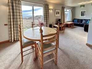Um quarto com uma mesa de jantar redonda de madeira, cadeiras, um sofá e vista para o exterior.