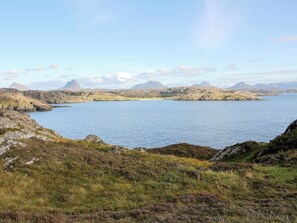 Un paysage côtier comprenant une étendue d’eau, un terrain rocheux et des montagnes à l’horizon.