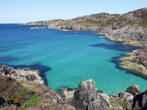 A coastal landscape with clear blue waters, rocky terrain, and sparse vegetation.