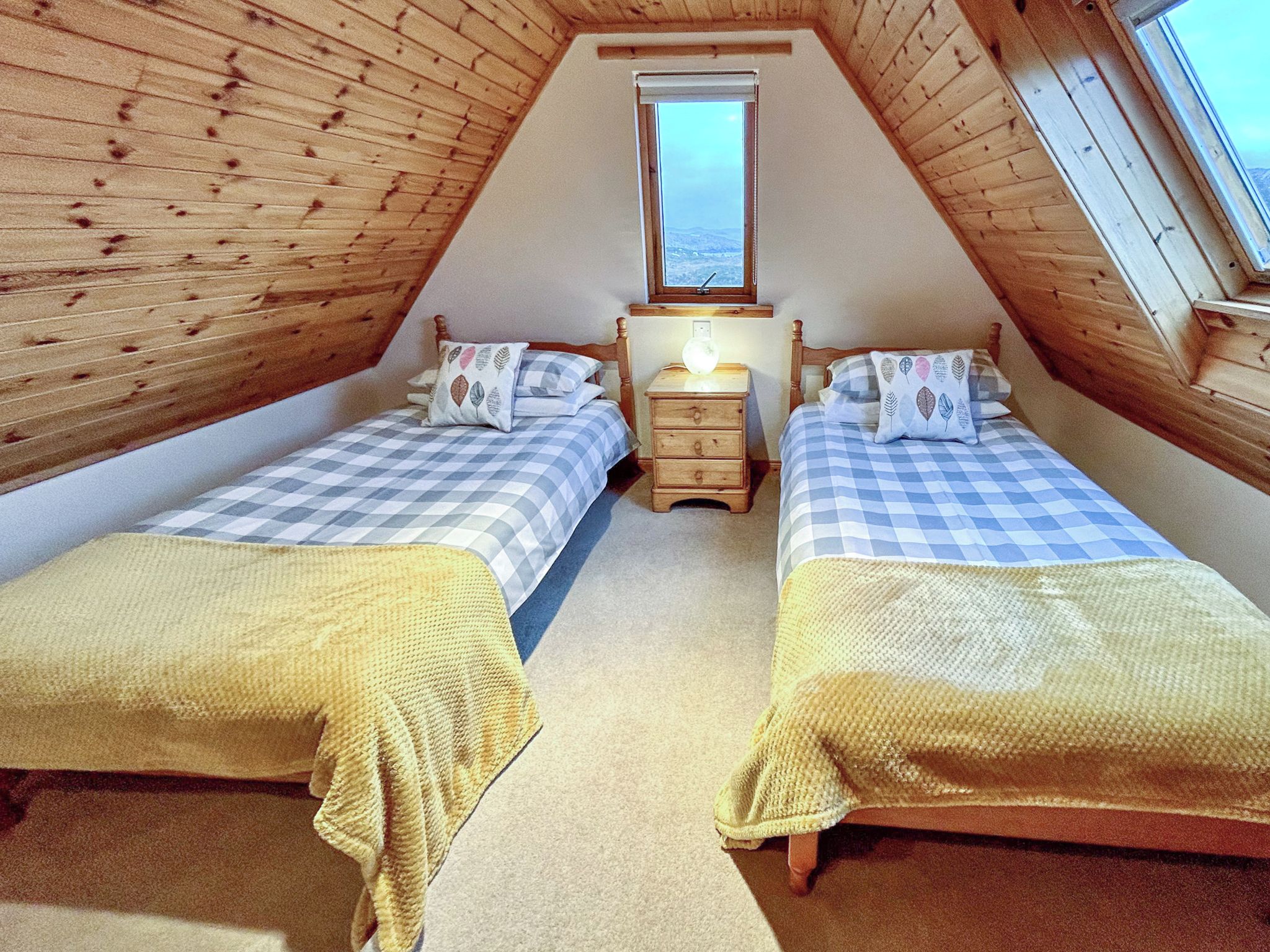 A small, cozy attic bedroom with two beds, a nightstand, and a window.